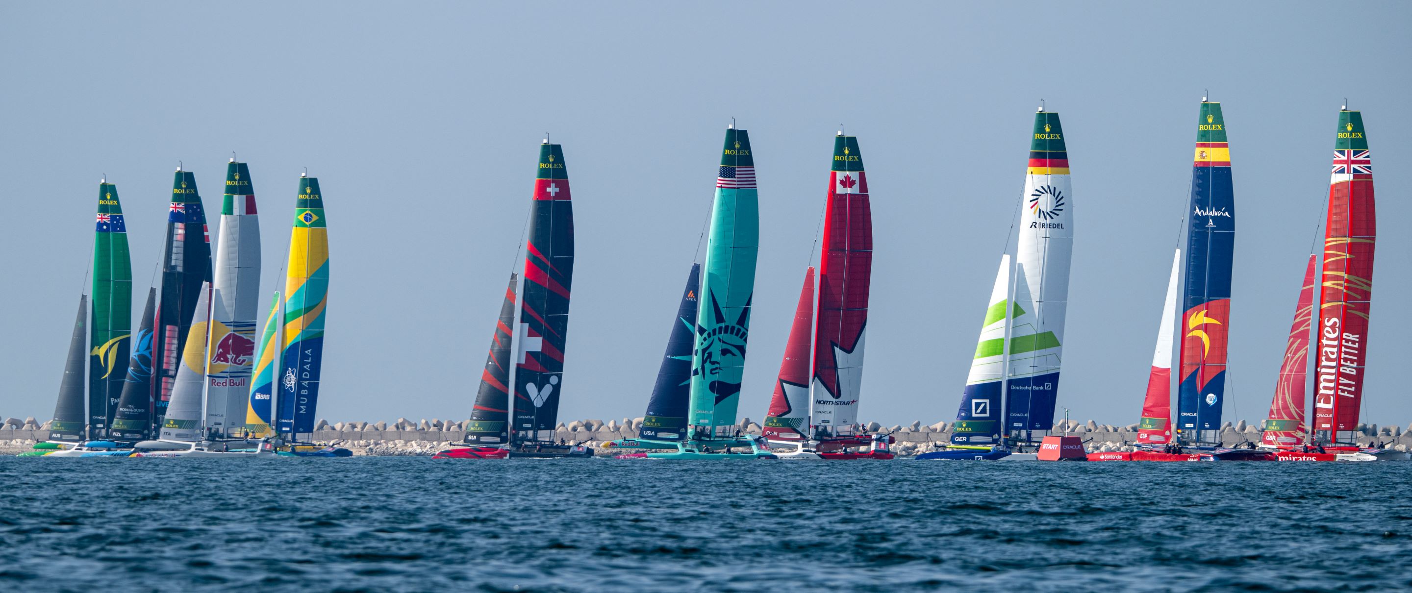 The colorful sails of catamarans line the horizon as the SailGP gets underway. 
