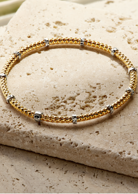 A yellow gold popcorn link bracelet with white gold stations on a flat stone surface.