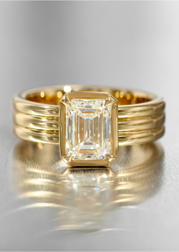 Triple shank yellow gold engagement ring with a bezel-set emerald cut diamond