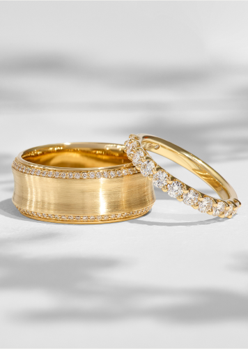Two yellow gold bridal bands with diamonds shine amid shadows on a white background. 